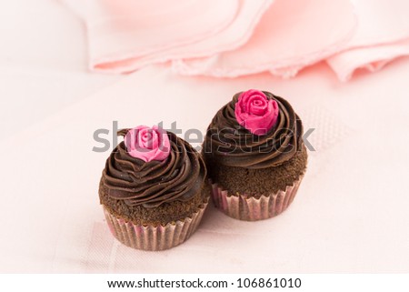 Two chocolate cupcakes decorated wit red and pink roses over a pink tablecloth