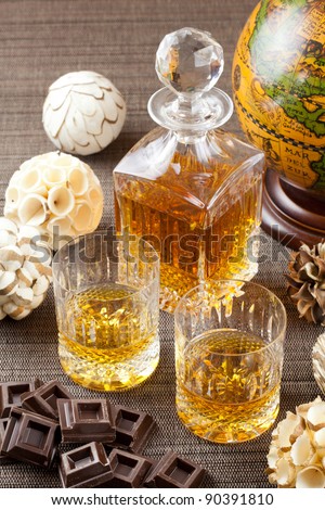 Dark chocolate and fine whiskey in crystal bottle and tumbler glasses with stylish spheres and antique globe in background