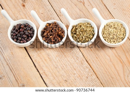 Assorted dry herbs and spices in white bowls over a wooden table