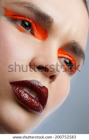 Close-up face shot of a woman with red lips and orange eyeshadows
