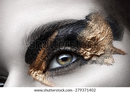 Eye with long eyelashes and black and gold makeup closeup