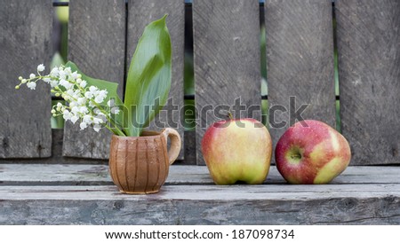 Red apples and lily of the valley flower in a ceramic small mug with old wood background