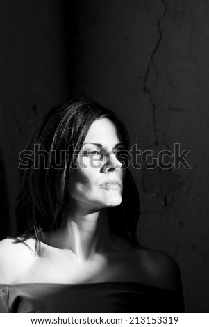Black and white shot of a beautiful, brunette woman in an old, abandoned house looking sad and melancholic