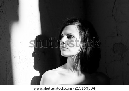Black and white shot of a beautiful, brunette woman in an old, abandoned house looking sad and melancholic