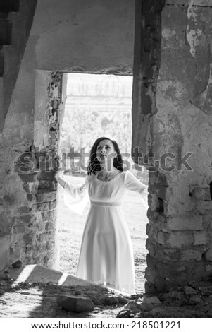 Beautiful, brunette woman in an old, abandoned house, wearing a wedding dress, posing with sunset light. Photo has grain texture visible on its maximum size. Artistic black and white photography