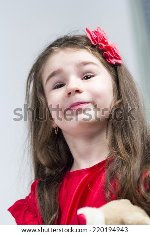 Beautiful little girl with long, curly hair and red dress posing with light grey background