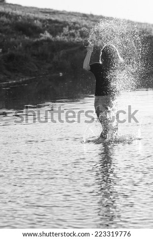 Beautiful girl with long, straight hair posing and playing with water in a small river. Black and white, artistic photography