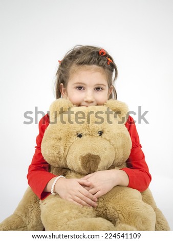 Beautiful little girl dressed in red playing with toy bear and posing with light grey background