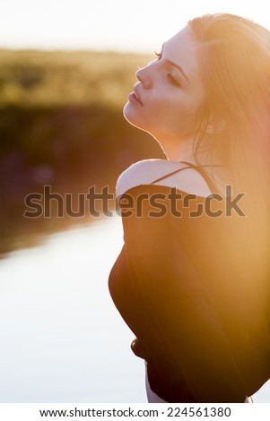 Beautiful girl with long, straight hair posing in the field with sunset light, against the light