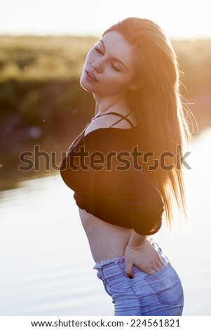 Beautiful girl with long, straight hair posing in the field with sunset light, against the light