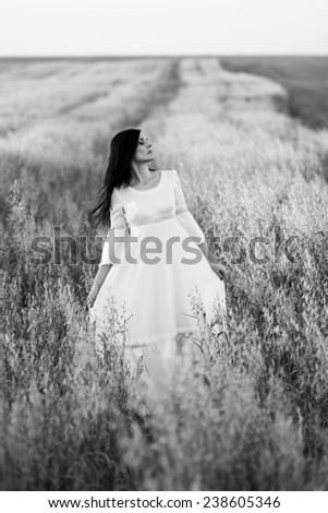 Brunette girl in the field, wearing a white dress, looking sad and worried. Photo has grain texture visible on its maximum size. Artistic black and white photography