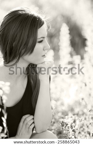 Black and white photo of beautiful girl with long, straight hair posing in the field looking melancholic