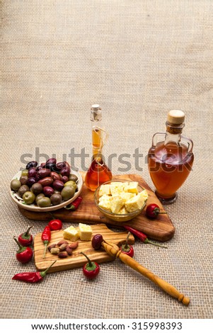Composition with olive wood, olives, cheese pieces in olive oil, vinegar and spices and burlap texture in the background