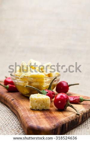 Composition with cheese pieces in olive oil and hot peppers on an olive wood cutting board