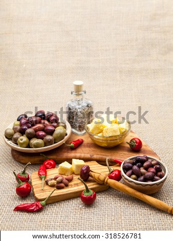 Composition with olive wood, olives, cheese pieces in olive oil, spices and burlap texture in the background