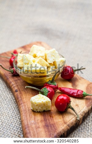 Composition with cheese pieces in olive oil and hot peppers on an olive wood cutting board