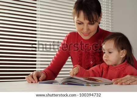 A nice Caucasian mom and daughter holding book on a light background