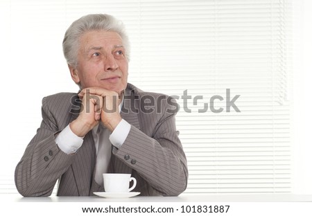 An elderly man with a cup sitting on light background