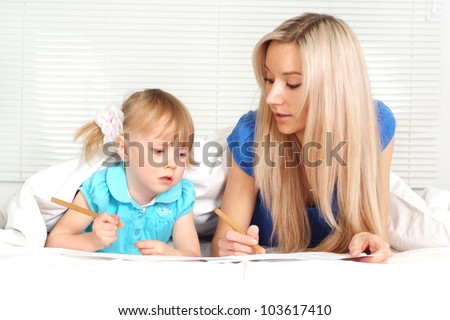 Beautiful caucasian mother and daughter lying on the bed with a pencils