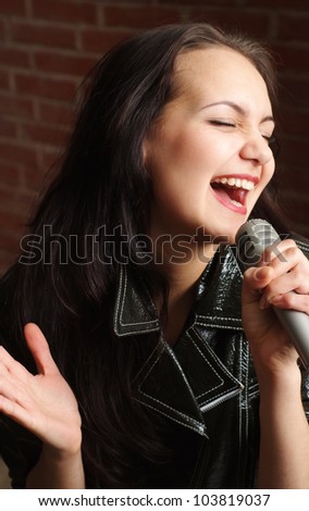 Beautiful lady with a microphone singing against a brick wall