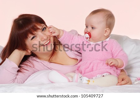 A pretty Caucasian mama with her daughter lying in bed on a light background
