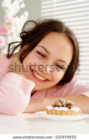Beautiful nice woman is and looks at a cake on a light background