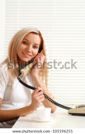 Beautiful Caucasian woman sitting with a phone on a light background
