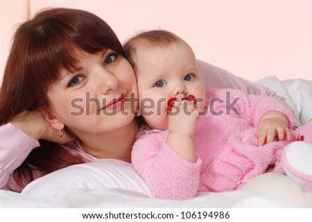 A beautiful mom with her daughter lying in bed on a light background