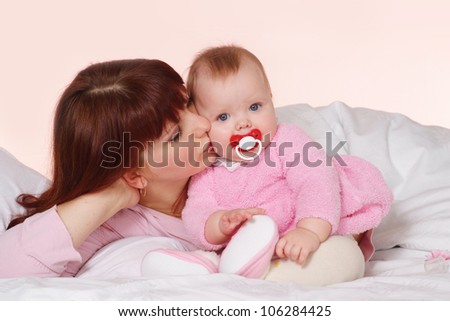 A good Caucasian mama with her daughter lying in bed on a light background