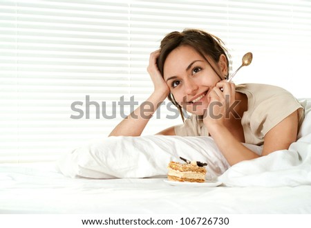 Beautiful nice girl lying on a bed with a cake on a light background