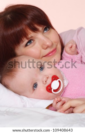 A beautiful mummy with her daughter lying in bed on a light background