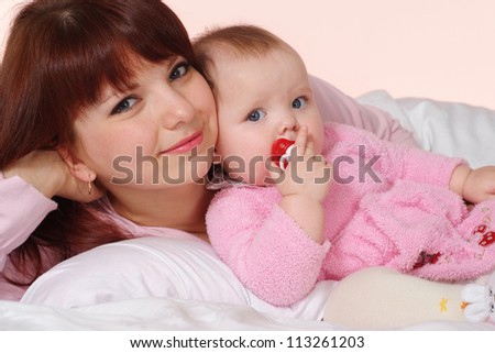 A luck Caucasian mom with her daughter lying in bed on a light background