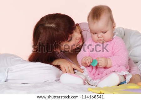 A beautiful happy mother with her daughter lying in bed on a light background