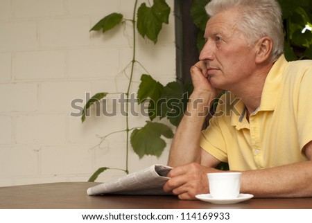 Adorable older man sitting at a table at home on the veranda