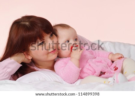 A good Caucasian mom with her daughter lying in bed on a light background