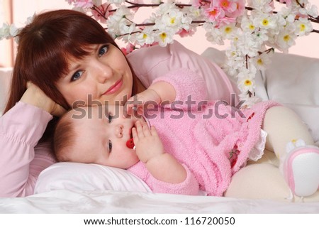A beautiful happy mom with her daughter lying in bed on a light background