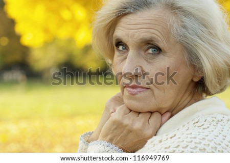 Beautiful old woman stands on a background of yellow leaves