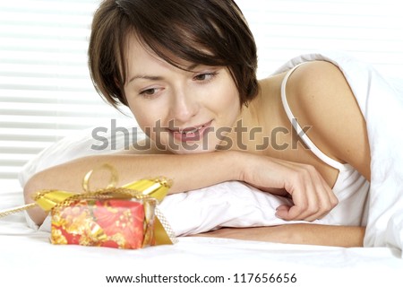 surprised young woman with a gift on a white bed