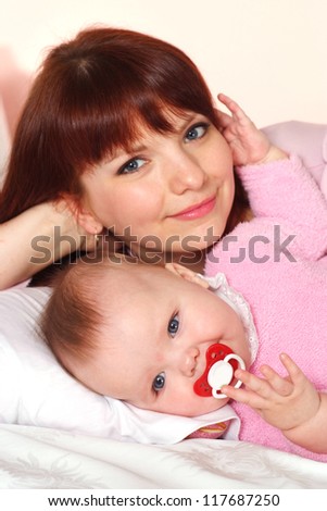 A good Caucasian mummy with her daughter lying in bed on a light background