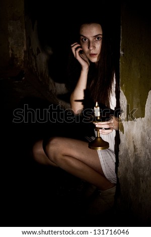 frightened young woman with a candlestick in a dark cellar