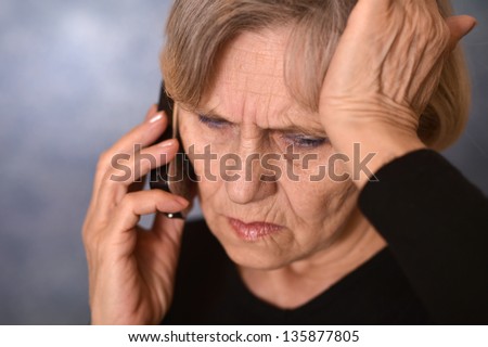 portrait of a sad old woman calling on a gray background