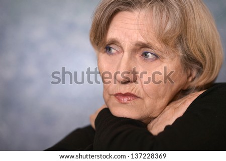 portrait of melancholy older woman in a black sweater on a gray background
