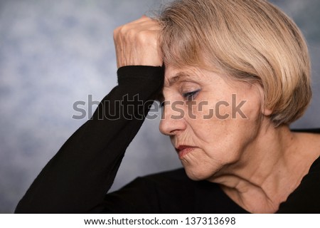 portrait of a sad older woman in a black sweater over gray background