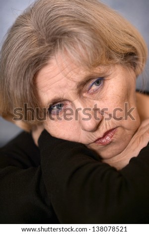 portrait of sadly older woman in a black sweater over gray background