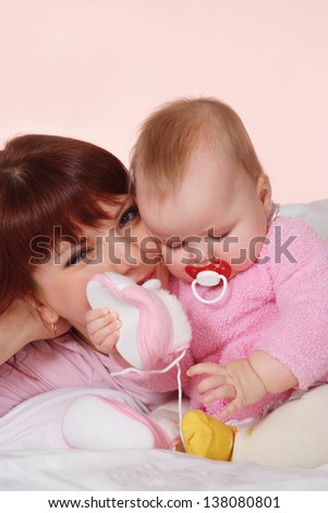 A beautiful nice mama with her daughter lying in bed on a light background