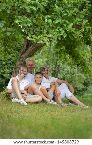 elderly man and woman with their grandchildren resting under a tree