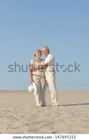 elder couple in love walking barefoot in the sand