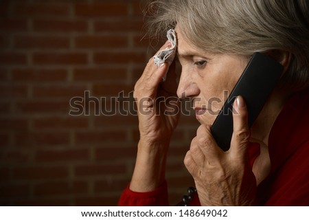 elder woman in red on a background of a brick