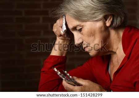 Older sick woman in red with pills on a background of a brick