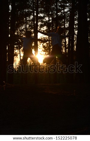 Two funny boys silhouettes in summer forest at sunset